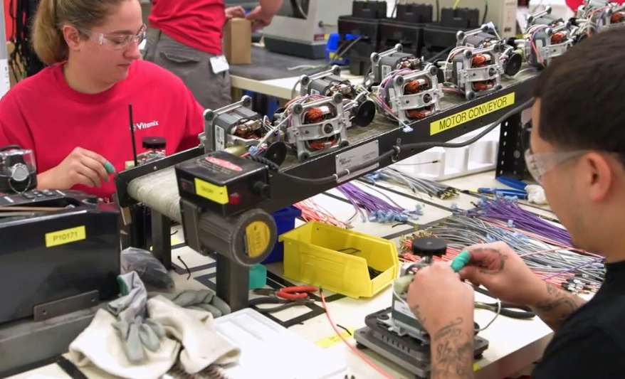 Workers assemble components beside a motor conveyor on a manufacturing line