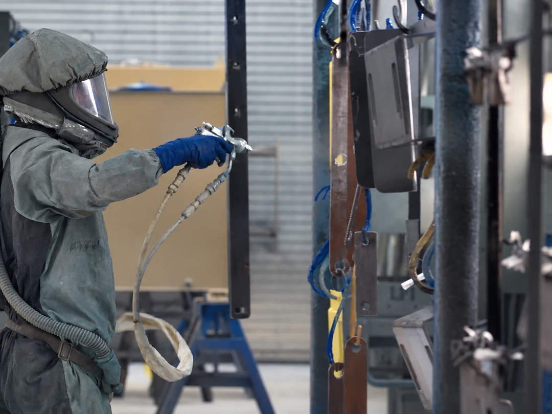 Worker spray-painting suspended metal parts